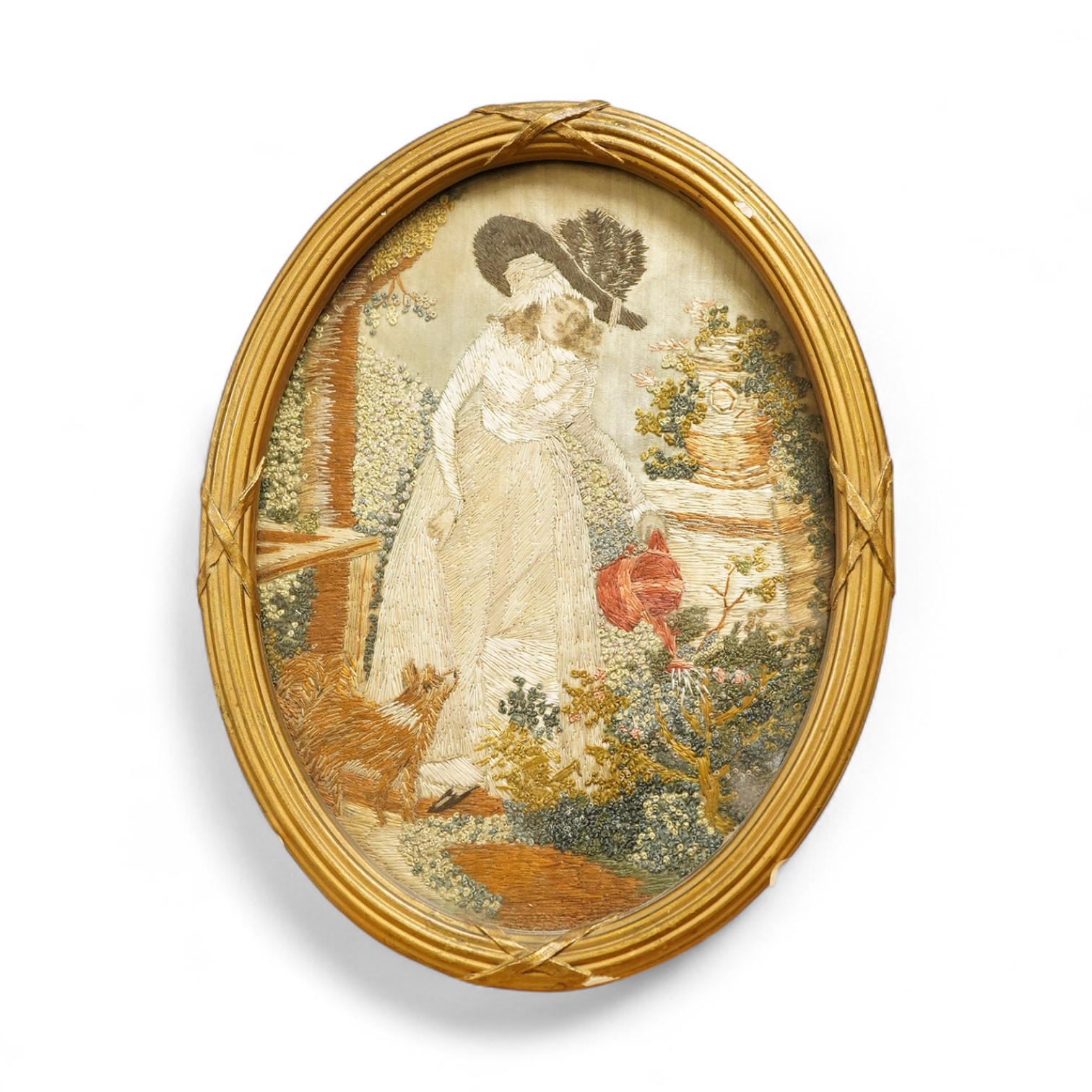 A small oval gilt framed late 19th century silk polychrome embroidery of a lady watering her garden with her dog at her side, 19cm high. Condition - good.